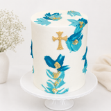 White cake with blue floral designs and a gold cross on a white stand.