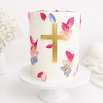 Decorative cake with floral designs and a gold cross on a white background
