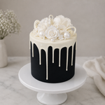 Black cake with white floral and pearl decorations on a marble surface.