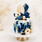 Decorative cake with blue and gold accents on a white stand against a light background