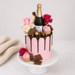 Pink cake with chocolate drizzle, flowers, and a bottle of champagne on a white background