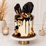 Decorative cake with chocolate drizzle and festive decorations on a marble stand.