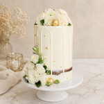 Decorative cake with white flowers and gold accents on a marble surface.