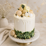 Decorative cake with white frosting, macarons, and flowers on a marble stand.