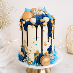 Decorative cake with chocolate drizzle, blue and gold elements on a white background