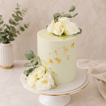 Green cake with white roses and gold accents on a stand, with a neutral background