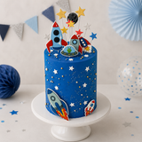 Blue space-themed cake with rocket designs on a white stand, decorated with stars and planets.