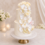 White wedding cake with floral decorations on a marble stand, set against a soft beige background.